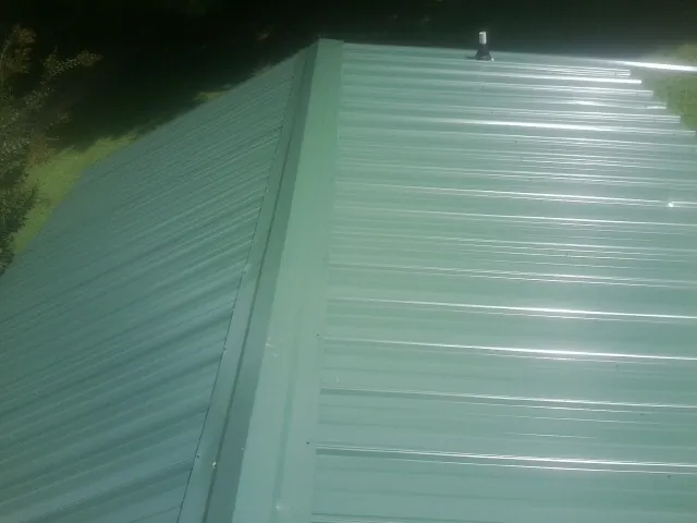 New green metal panels meeting at the ridge of a roof — Flat Roof Repair work by our crew in Fulton