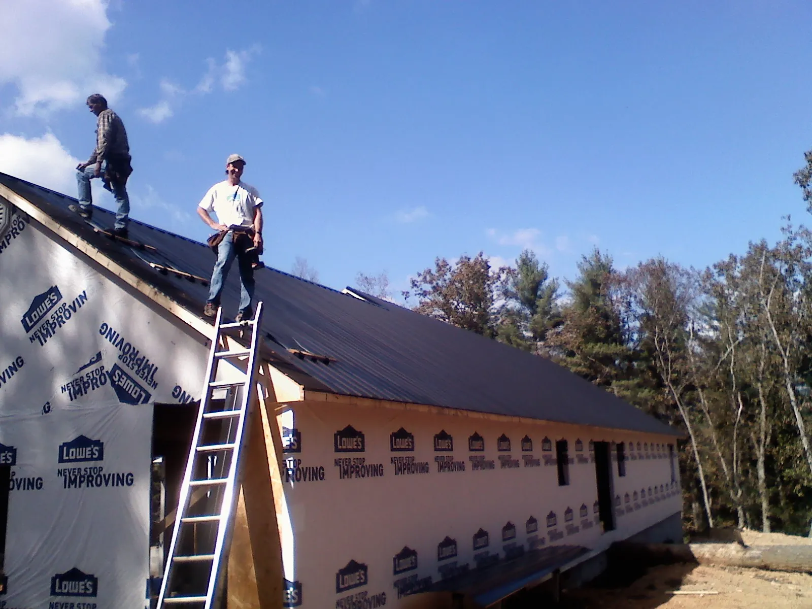 Two roofers standing on a long dark metal roof over a wrapped building in Fulton
