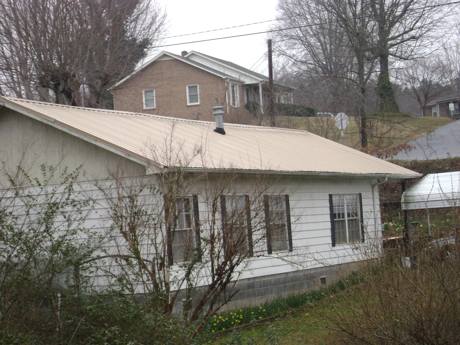Tan metal roof on a white sided house set into a hillside — Commercial Roofing by Roofing Brothers in Fulton